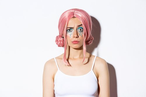 Close-up of confused girl in pink wig, raising eyebrow with suspicious expression, standing over white background.