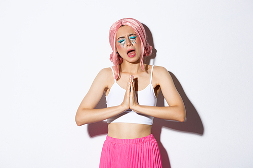 Image of cute party girl begging for help, holding hands together and pleading, asking for something, standing in halloween costume with pink wig and bright makeup.