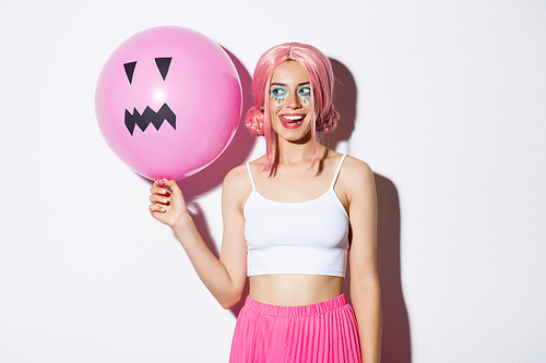 Image of coquettish party girl with bright makeup, wearing pink wig, holding balloon with Jack-o