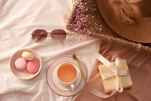 Cup of tea, macarons cake, gift box, glasses, hat and flowers on fabric background