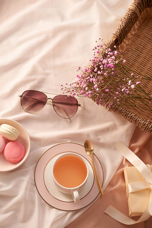 Cup of tea, macarons cake, glasses and flowers on fabric background