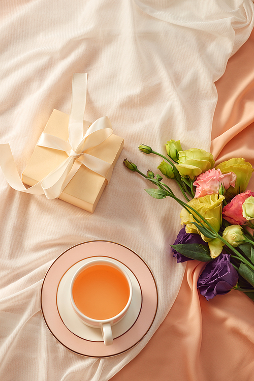 Fresh flowers with gift box and tea cup on light fabric background