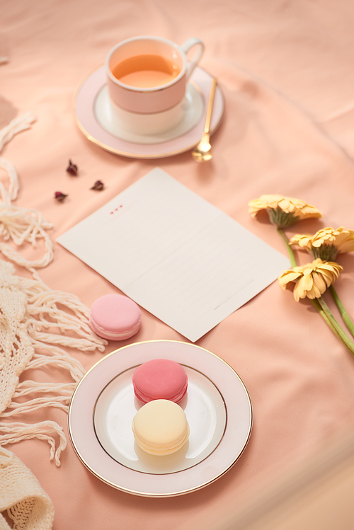 Envelope, flowers, and macarons with cup of tea on light background
