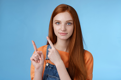 Assertive good-looking redhead girl know what talking about pointing upper left corner index fingers showing confidently good product recommend check out standing blue background. Copy space