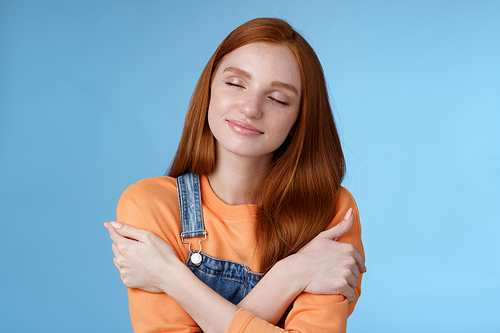 Passionate romantic tender ginger girl feel safe comfort close eyes smiling gently lovely daydreaming hugging herself recalling boyfriend cuddles sensual embraces, standing blue background happy.
