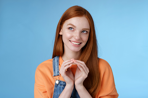 Devious tricky smart pretty redhead girlfriend have evil plan smirking mysteriously look upper left corner twiddles fingers think excellent plan, smiling delighted, standing blue background.