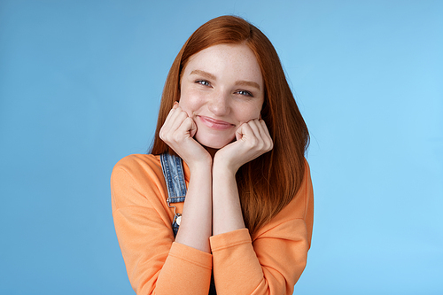 Tenderness, wellbeing, beauty conept. Attractive young ginger girl pure skin blue eyes lean palms silly smiling camera look amused enthusiastic listen interesting stories gladly, blue background.