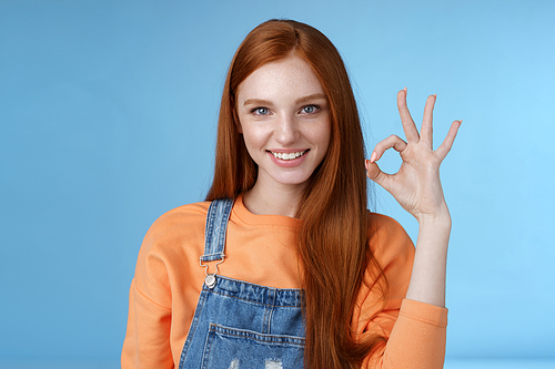 Sassy confident redhead girl got under control show okay ok excellent gesture cheeky look camera grinning assertive assuring everything awesome give permission approve good product, blue background.