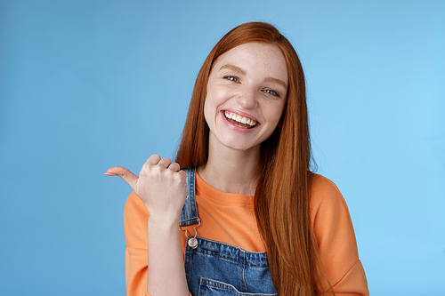 Lifestyle. Girl introducing her friend pointing thumb left smiling laughing joyfully proudly telling pros cool product recommend telling about cozy cafe tasty coffee having fun posing blue background.