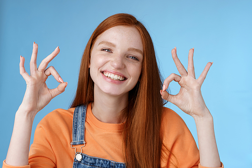 Wellbeing, happiness, perfection concept. Attractive friendly smiling joyful redhead female student show excellent okay ok gestures grinning approval agree awesome concept, satisfied blue background.