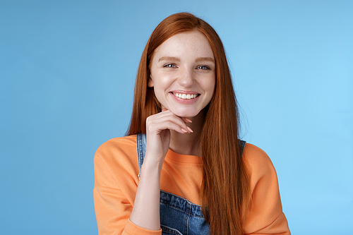 Stylish confident happy smart creative redhead girl look delighted thoughtful like interesting suggestion touch chin smiling approval friendly talking, standing blue background wear overalls.