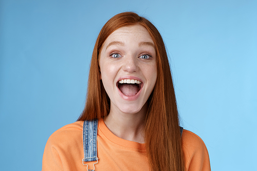 Lifestyle. Amused charismatic lively outgoing ginger girl thrilled having fun friends yelling say a showing perfect white smile enjoy friendly joyful atmosphere standing excited positive blue background.