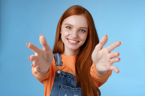 Come into arms. Charming sincere happy kind redhead girl baby sitting stretch hands camera wanna hold catch smiling friendly asking pass object, standing blue background reach friend give cuddles.