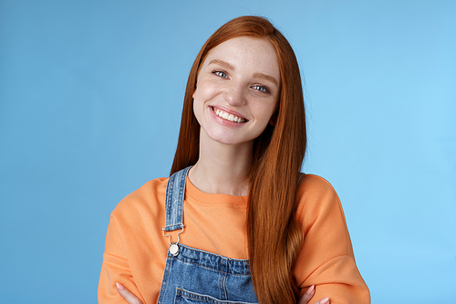 Charismatic kind pleasant redhead girl blue eyes smiling friendly listen politely customer standing blue background tilting head amused grinning cross hands chest professional confidence pose.