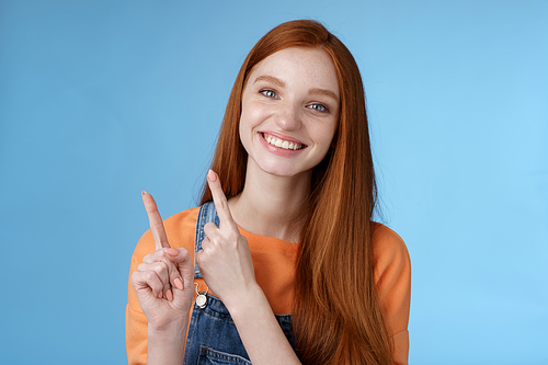 Lifestyle. Happy tender redhead girl sincerely smiling white teeth helpful look camera excited give hand pointing upper left corner introduce sale offer recommend try promo standing blue background.