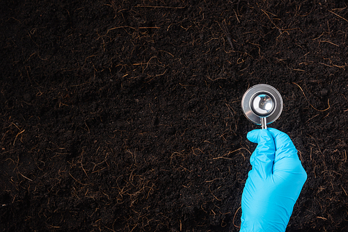 Hand of researcher woman wear gloves holding a stethoscope on fertile black soil for check condition before agriculture or planting, Concept of World Soil Day, Earth day and hands ecology environments