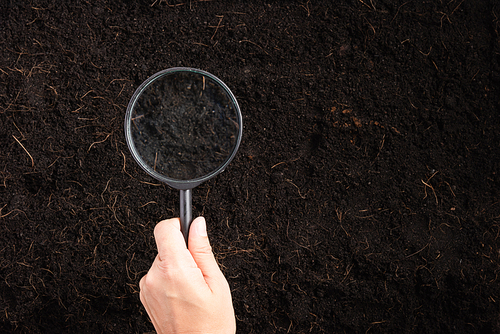 Top view the hand of researcher woman holding a magnifying glass on black soil at the garden to research, Concept of global pollution, Save Earth and World Soil Day