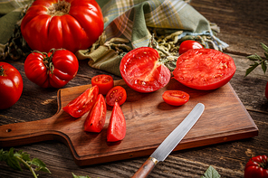 Whole red tomatoes and slice of tomatoes on wooden cutting board