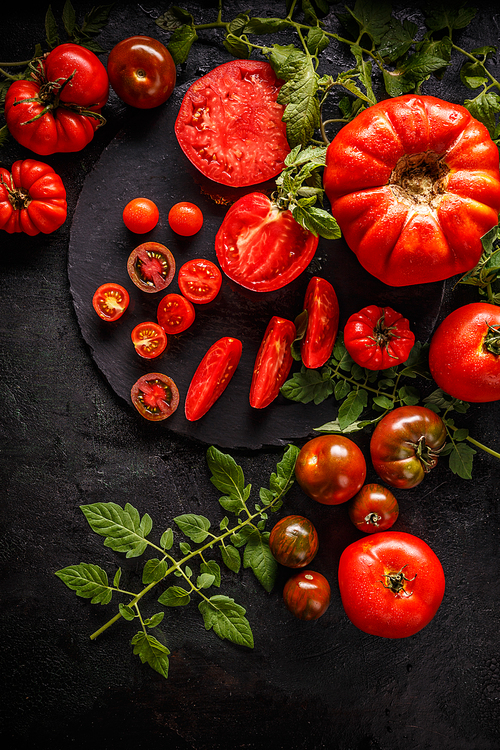 Whole red tomatoes and slice of tomatoes on black background