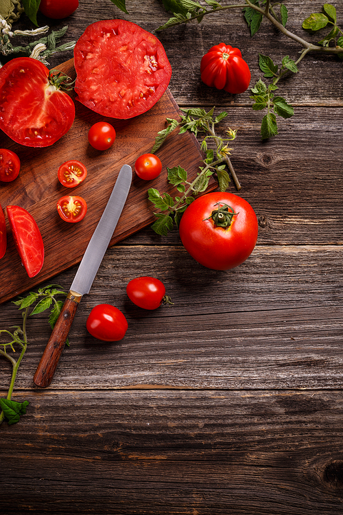 Different juicy tomatoes and slices on wooden background, copy space