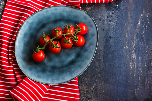 Fresh ripe organic cherry tomatoes and bright ceramic plates on dark wooden table wt copyspace