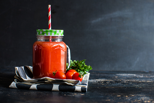 Organic tomatoes juice in a bottle with straw and fresh cherry tomatoes and parsley herb on dark wooden table