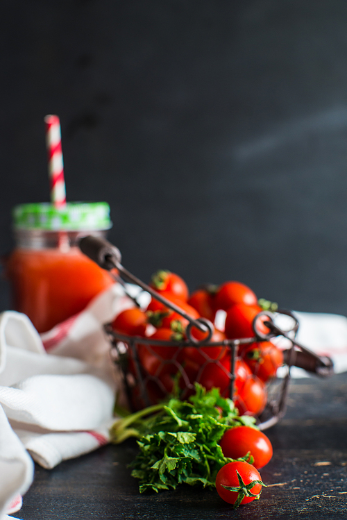 Organic tomatoes juice in a bottle with straw and fresh cherry tomatoes and parsley herb on dark wooden table