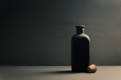 A single black ceramic bottle with the plug off over a dark background