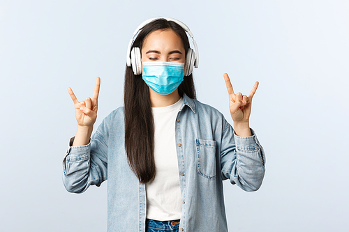 Social distancing lifestyle, covid-19 and self-isolation leisure concept. Carefree happy smiling asian teenage girl having fun listening awesome music in wireless headphones, show rock-n-roll gesture.