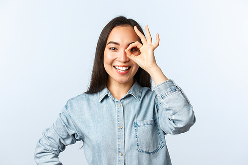 Lifestyle, people emotions and beauty concept. Optimistic smiling asian girl looking through okay sign happy, assure everything under control. all good, recommend best product.