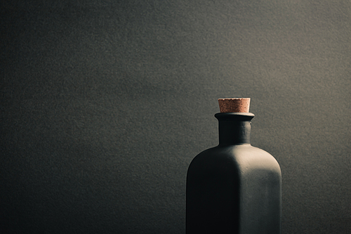 A close up of a black ceramic bottle with a dark background