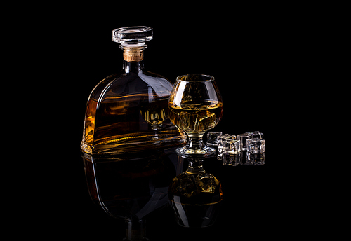 Glass of brandy with ice cubes and bottle on black background