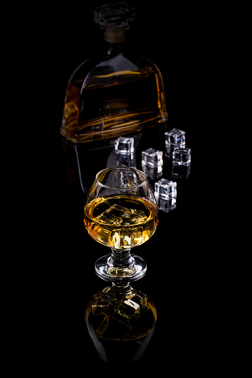 Glass of brandy with ice cub and bottle