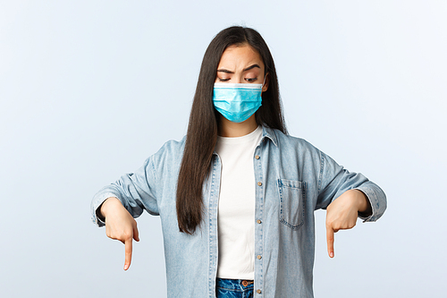 Social distancing lifestyle, covid-19 pandemic everyday life and leisure concept. Skeptical and confused asian woman in medical mask, casual clothes, looking and pointing down.