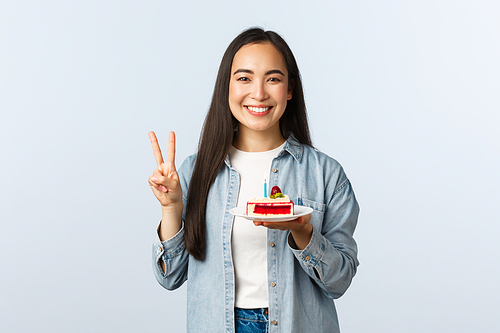 Social distancing lifestyle, covid-19 pandemic, celebrating holidays during coronavirus concept. Happy smiling asian birthday girl holding bday cake and show peace sign.
