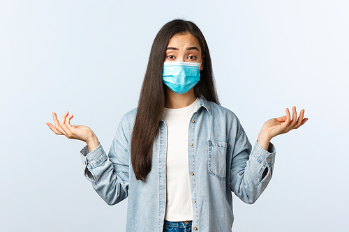 Social distancing lifestyle, covid-19 pandemic everyday life and leisure concept. Confused attractive asian woman in medical mask dont know, shrugging shoulders clueless.