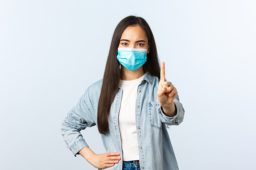 Social distancing lifestyle, covid-19 pandemic everyday life and leisure concept. Angry displeased asian girl in medical mask scolding person, show finger, prohibit or warning someone.