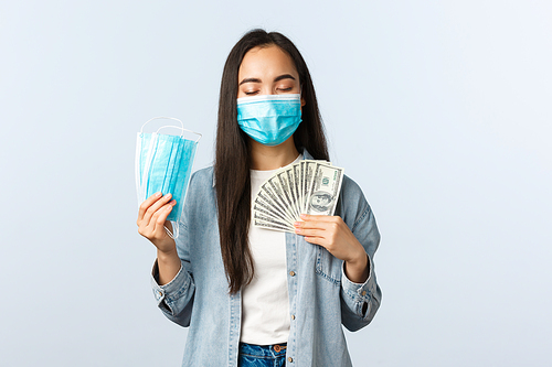 covid-19 pandemic, coronavirus expences and finance concept. Satisfied greedy asian girl in medical mask hugging money and showing masks, earn cash during coronavirus lockdown.