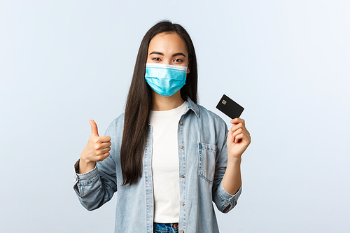 Social distancing lifestyle, covid-19 pandemic and contactless shopping concept. Satisfied asian female in medical mask show thumbs-up gesture and promote credit card features, bankc account.