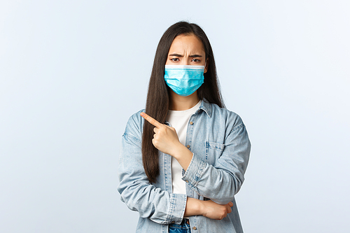 Social distancing lifestyle, covid-19 pandemic everyday life concept. Disappointed complaining female customer arguing with clerk, pointing finger upper left corner displeased, wear medical mask.