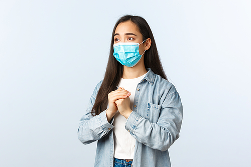 Social distancing lifestyle, covid-19 pandemic everyday life concept. Concerned hopeful asian woman worry about friend got positive test coronavirus, praying in medical mask, plead gesture.