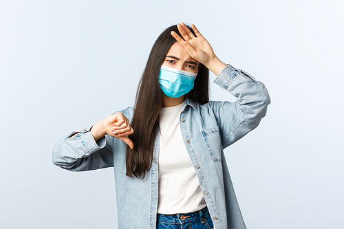 Social distancing lifestyle, covid-19 pandemic everyday life concept. Asian girl feeling bad, showing thumb-down as touching hot forehead, have high fever, wear medical mask, catch coronavirus.