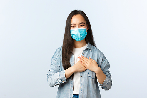 Social distancing lifestyle, covid-19 pandemic everyday life and leisure concept. Delighted happy asian girl being praised, feeling touched and thankful, touching heart, smiling in medical mask.
