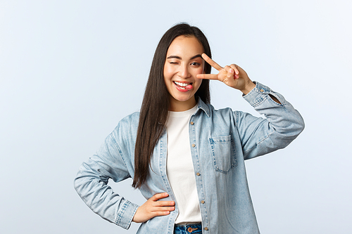 Lifestyle, people emotions and beauty concept. Carefree enthusiastic asian woman in casual clothes stay positive, show tongue and peace sign over eye, laughing happy.