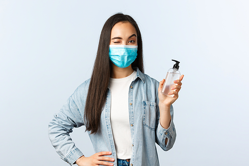 Social distancing lifestyle, covid-19 pandemic preventing virus concept. Cheerful asian woman in medical mask wink, encourage people use hand sanitizer and wash hands during coronavirus.