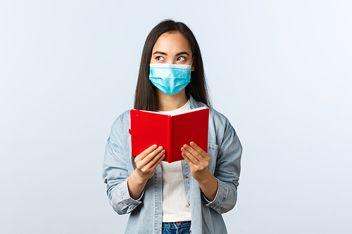Covid-19 pandemic, education during coronavirus, back to school concept. Thoughtful attractive asian girl in medical mask, female student reading notebook and look away thinking.