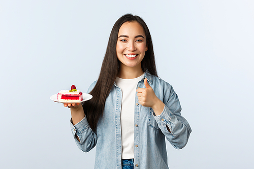 Social distancing lifestyle, covid-19 pandemic, celebrating holidays during coronavirus concept. Happy cheerful asian female show thumbs-up and smiling, holding delicious cake dessert.
