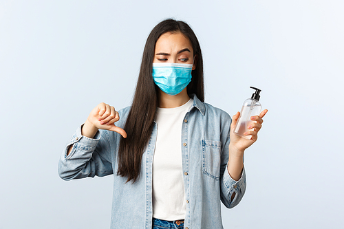 Social distancing lifestyle, covid-19 pandemic preventing virus concept. Disappointed asian woman in medical mask disapprove and judge bad product, show awful hand sanitizer, thumbs-down.