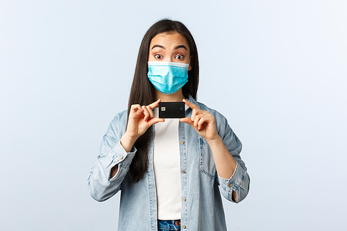 Social distancing lifestyle, covid-19 pandemic and contactless shopping concept. Cheerful asian girl in medical mask recommend using credit card, open bank account or place deposit.