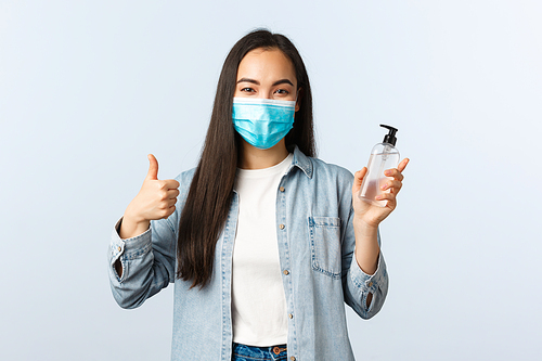 Social distancing lifestyle, covid-19 pandemic preventing virus concept. Cheerful asian woman in medical mask show thumb-up, encourage people use hand sanitizer and wash hands during coronavirus.
